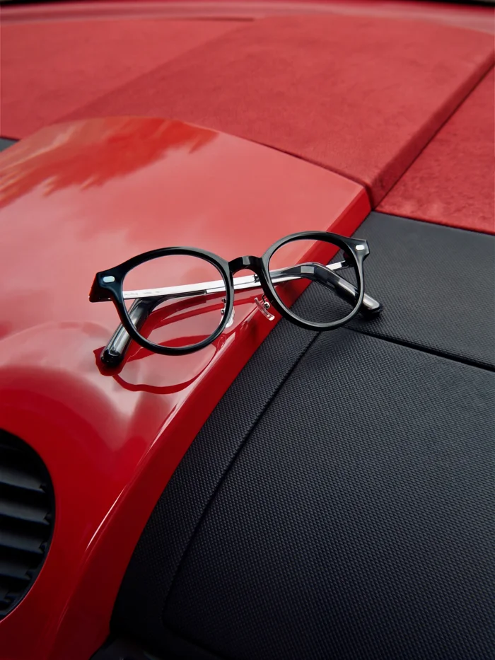 The NIMO frame resting on the glossy red bodywork of a sports car, its silver temple catching the light