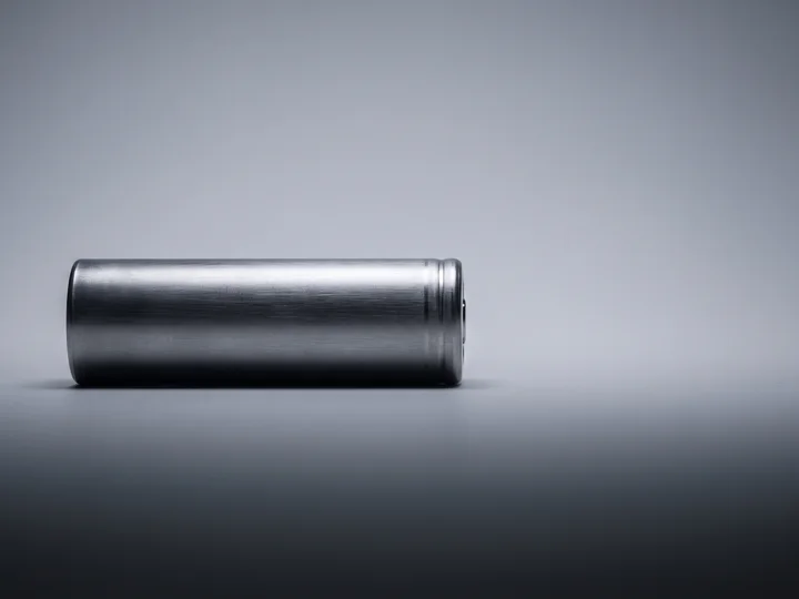 A brushed steel-shell battery cell resting on a seamless grey studio background