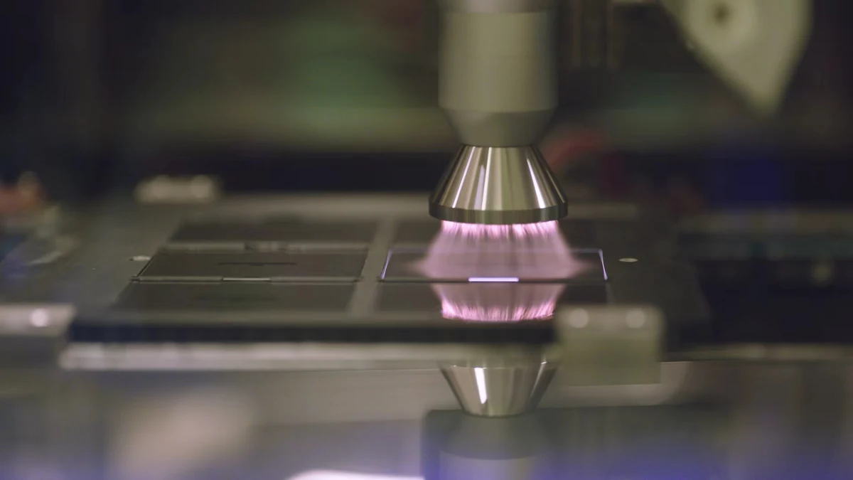 A waveguide plate under a processing head on the production line, lit violet